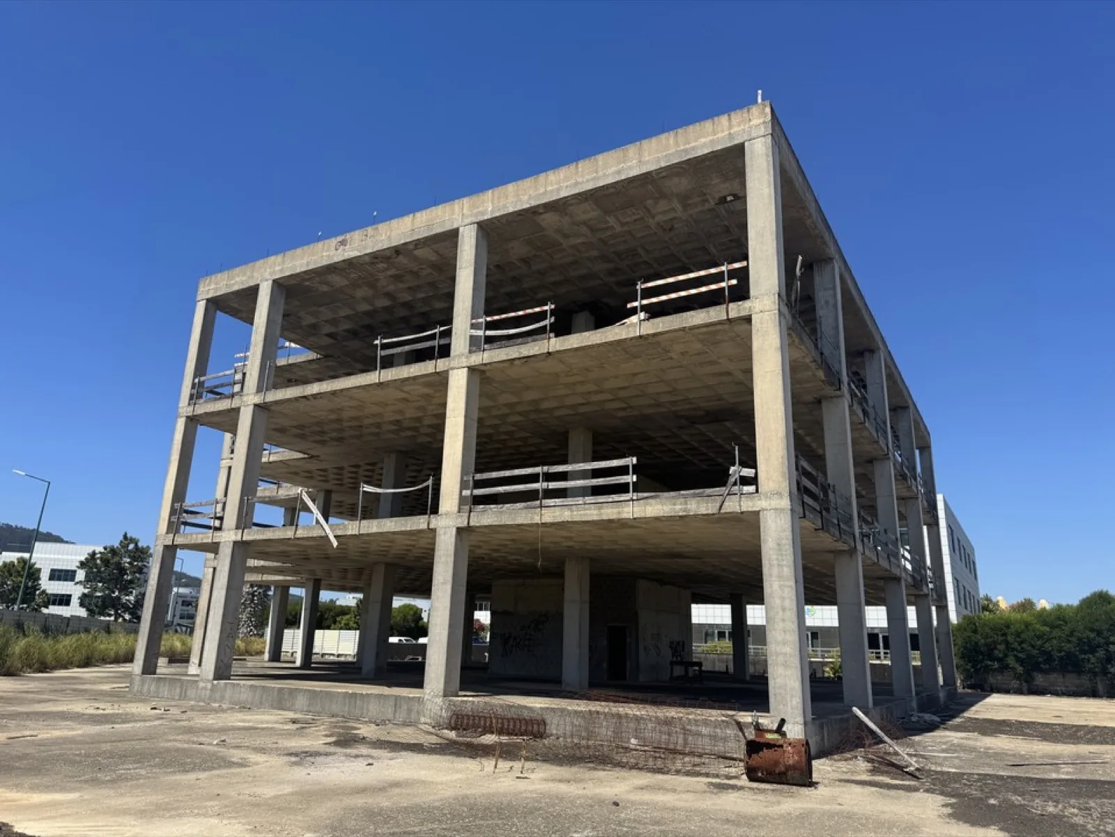 An empty three-storey reinforced concrete frame under a blue sky.